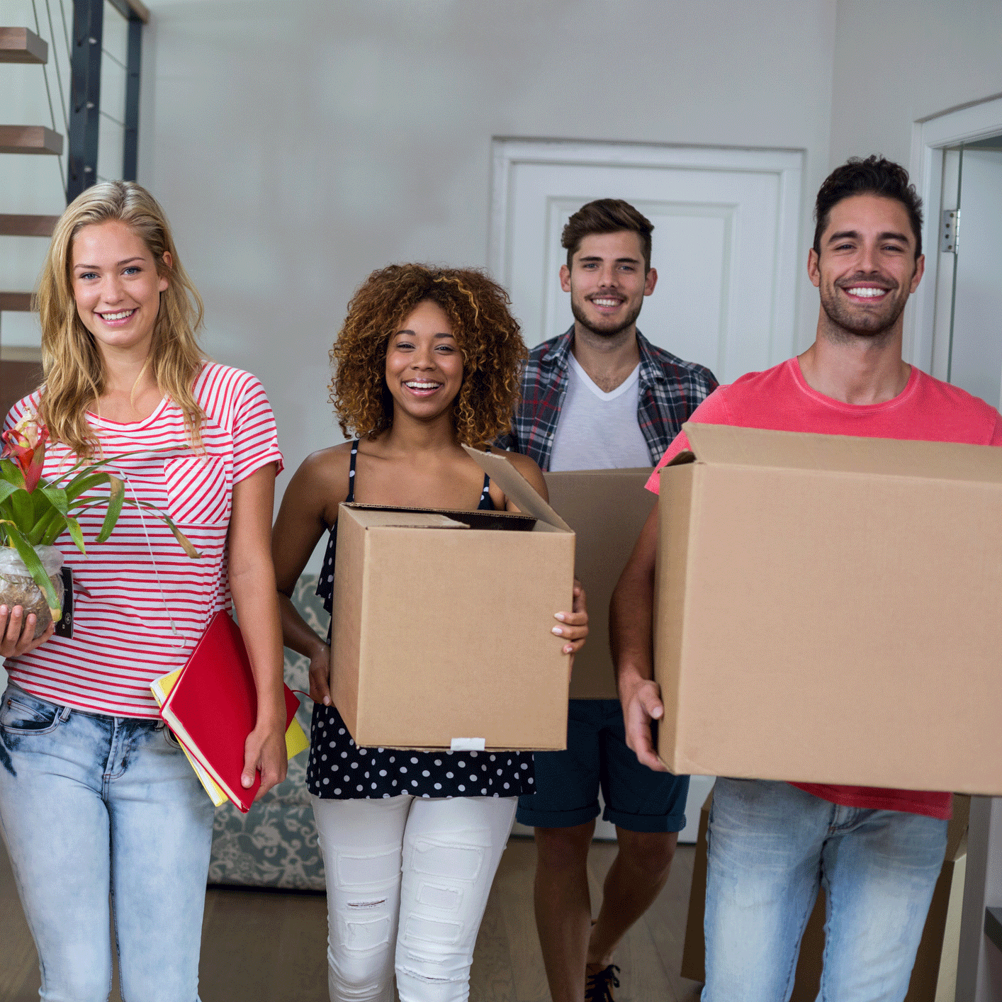 Four students holding moving boxes ready to move into their apartment